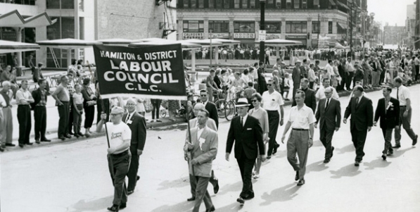 Delegation from the Hamilton & District Labour Council marching west at Market Square. Mayor Victor Kennedy Copps is in the white hat marching behind the banner. King William Street and the Lister building are in the background. Delegation from the Hamilton & District Labour Council marching west at Market Square. Mayor Victor Kennedy Copps is in the white hat marching behind the banner. King William Street and the Lister building are in the background.